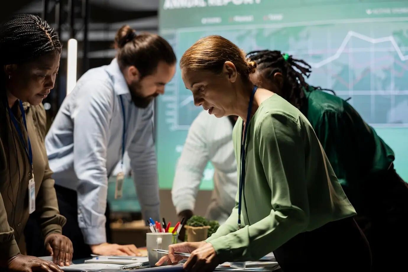 Eine vielfältige Gruppe von Mitarbeitenden, die nach Feierabend mithilfe von Projektionen an einem Unternehmensbriefing zusammenarbeitet und